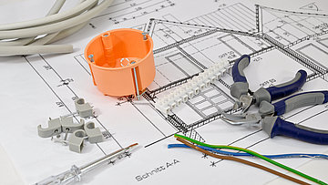Auf der Querschnittszeichnung eines Hausneubaus liegen Werkzeuge zur Elektroinstallation.